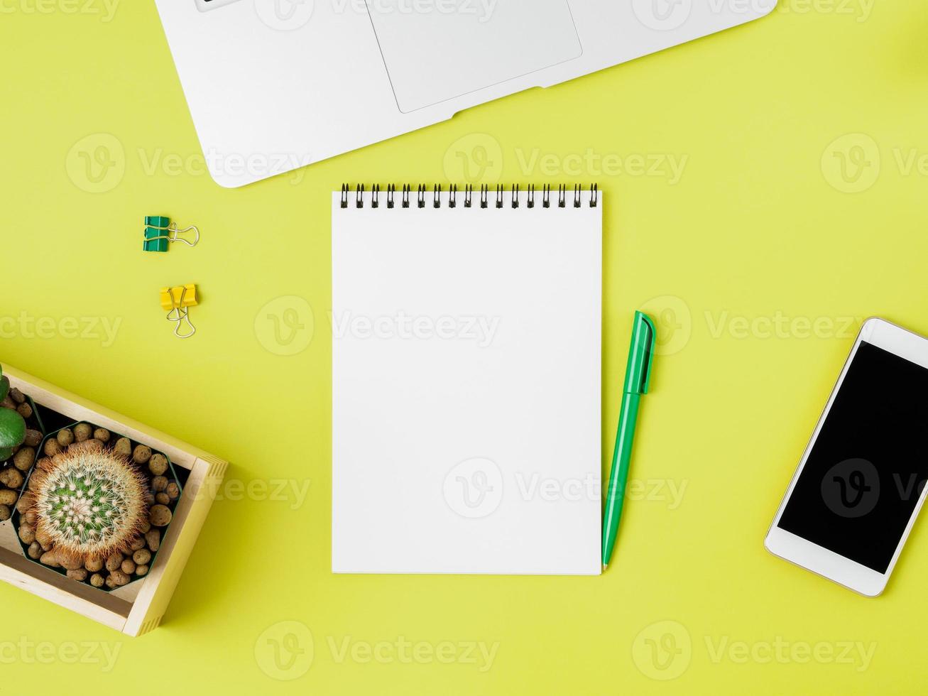 Top view of modern bright yellow office desktop with blank notepad, computer, smartphone. Mock up, empty space photo