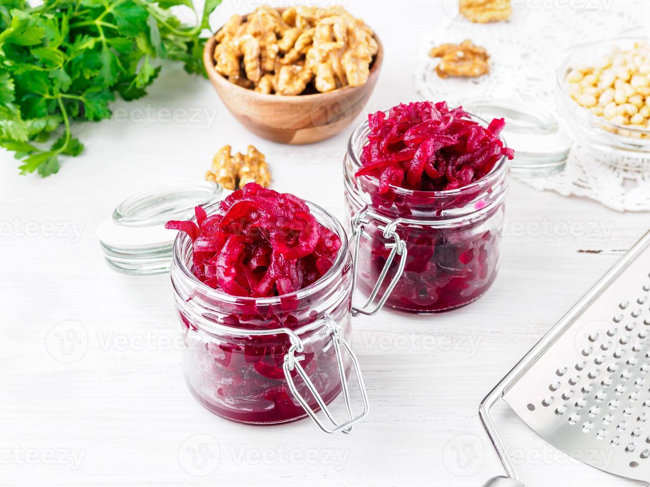 Fresh salad of grated boiled beetroot in jars, white wooden background, side view. photo