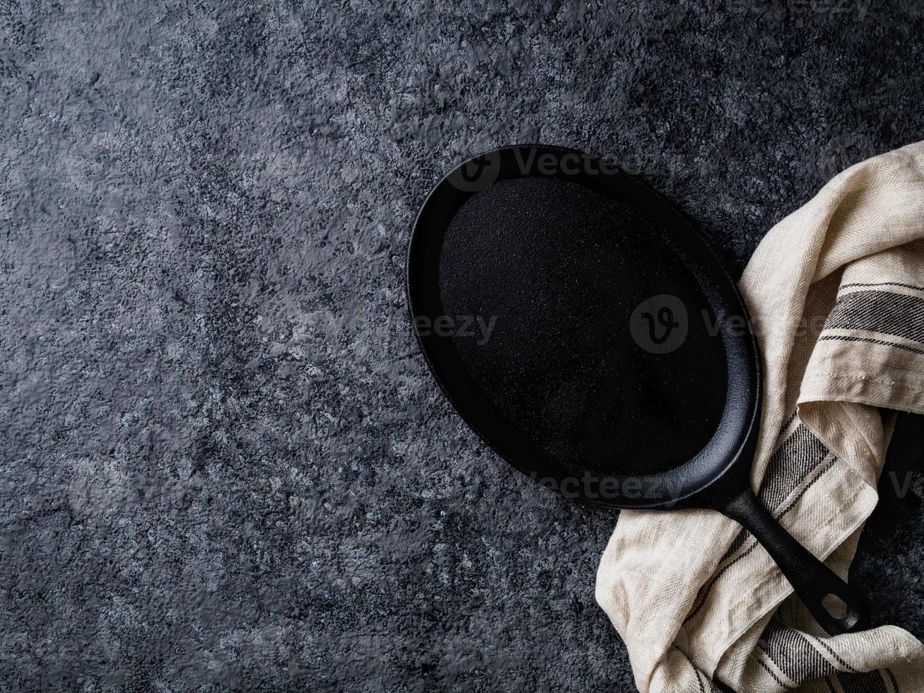 empty oval cast iron frying pan on dark grey concrete background, top view, blank space for text photo