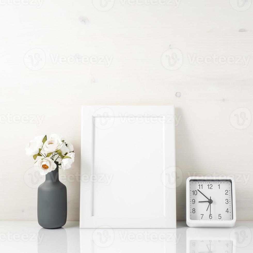 marco blanco, flor en jarrón, reloj en mesa blanca contra el wh foto