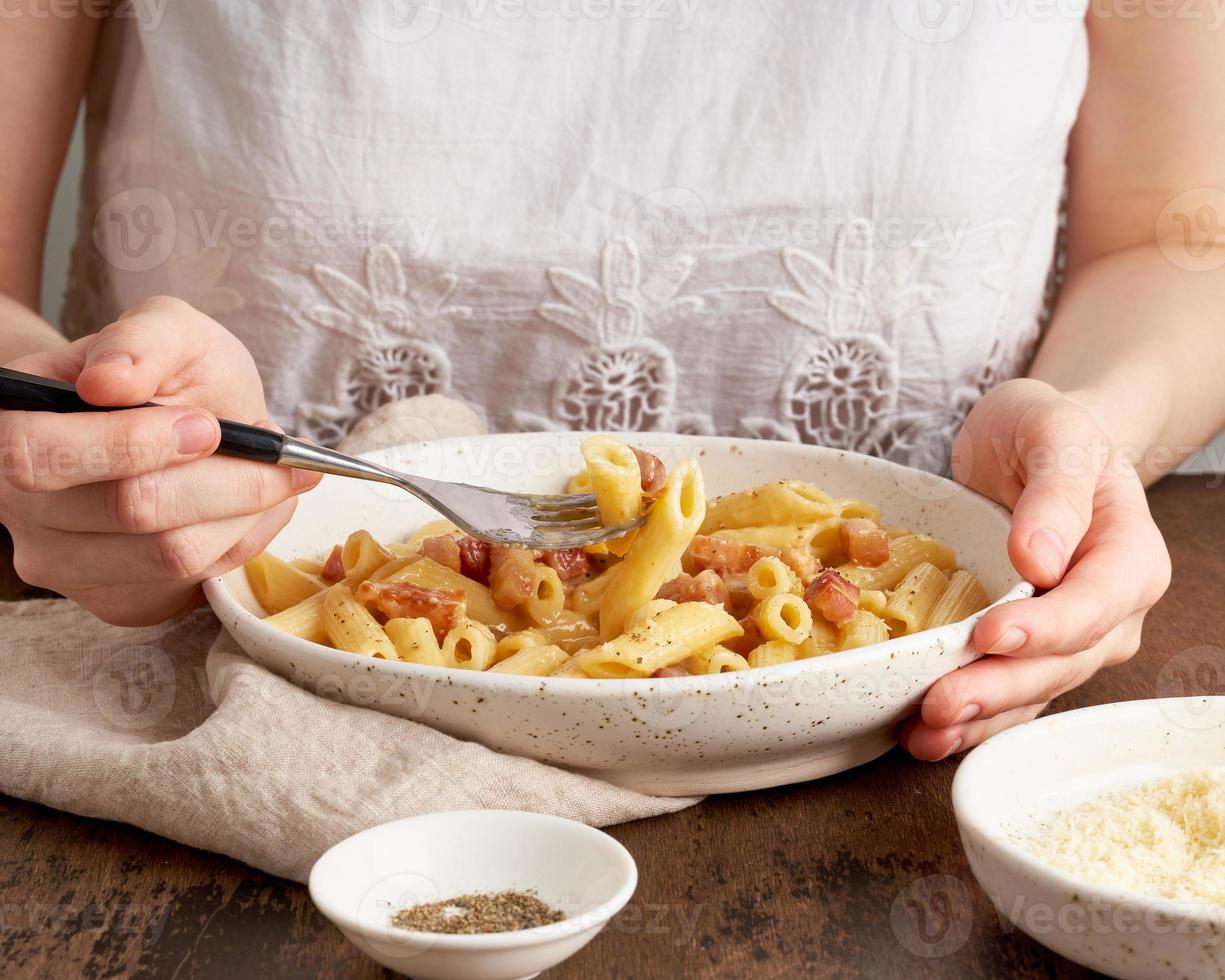 pasta carbonara. la mujer se sienta a la mesa y come pasta penne con panceta, foto