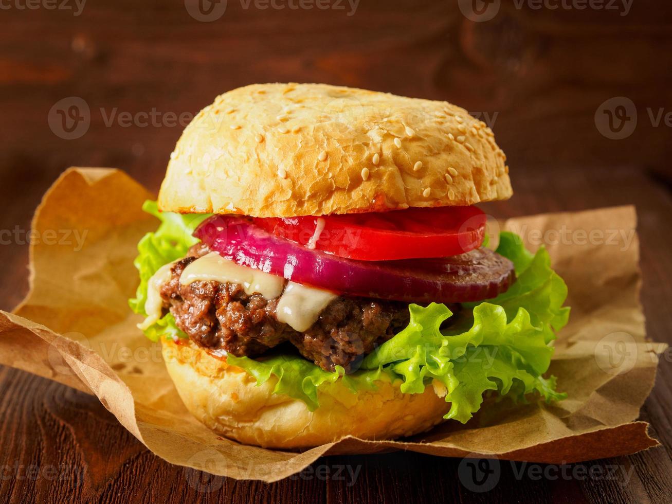 Big delicious homemade burger with beef cutlet, cheese, onion, tomato and lettuce on toasted rolls. American fast food, unhealthy eating. Side view, selective focus photo