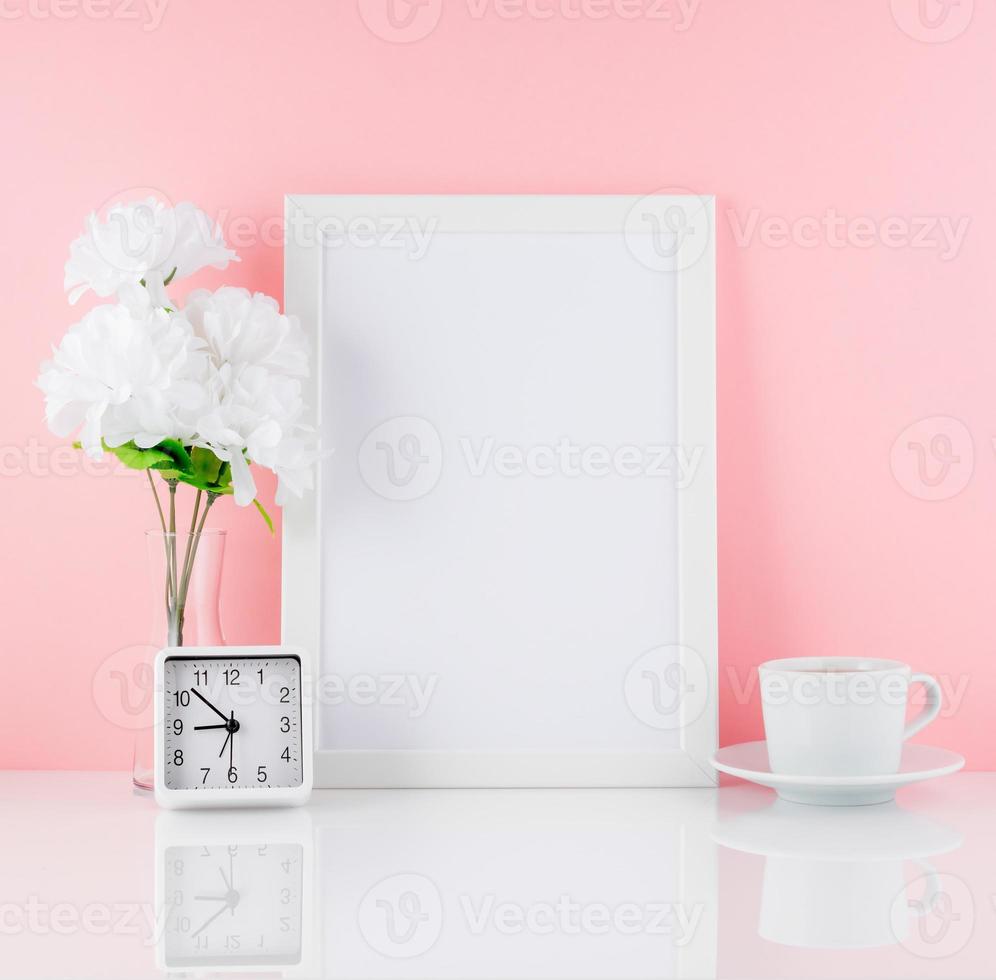 marco blanco en blanco, flor, reloj, taza de café o té en una mesa blanca contra la pared rosa con espacio para copiar. Bosquejo. foto