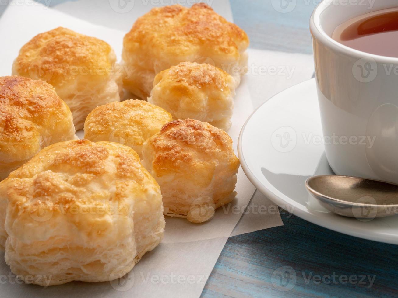 deliciosos panecillos de exuberante hojaldre sin levadura sobre papel pergamino sobre una mesa de madera azul, vista lateral. desayuno con una taza de té y pasteles caseros por la mañana. foto