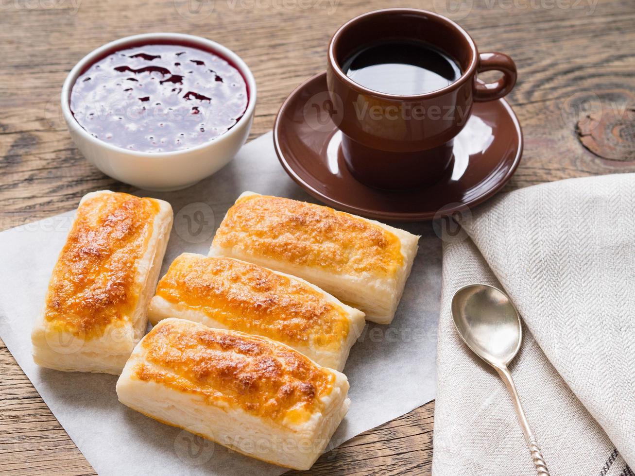 Breakfast of sweet rolls from puff pastry, raspberry jam, cup of coffee on parchment paper. photo