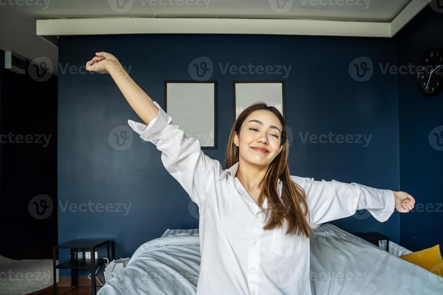 Happy mixed race girl waking up in her bed in morning after good night sleep, feeling energetic, stretching arms and back. photo