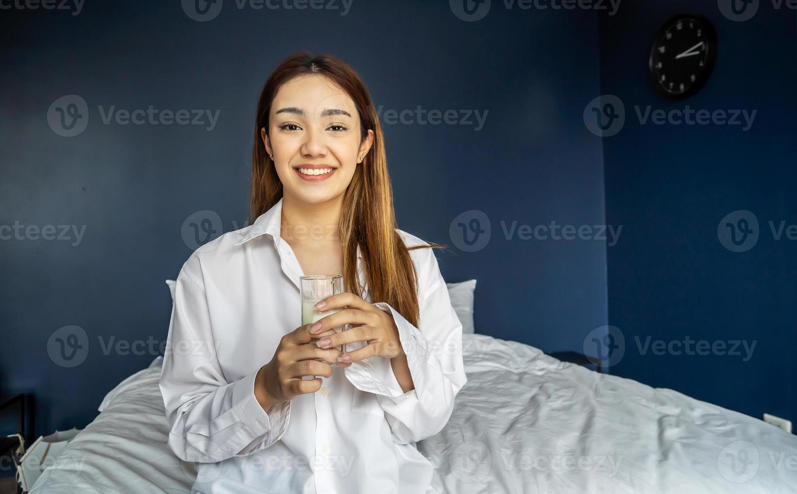 Young woman is lying on her bed smiling while holding a glass of milk, Healthy refreshment photo