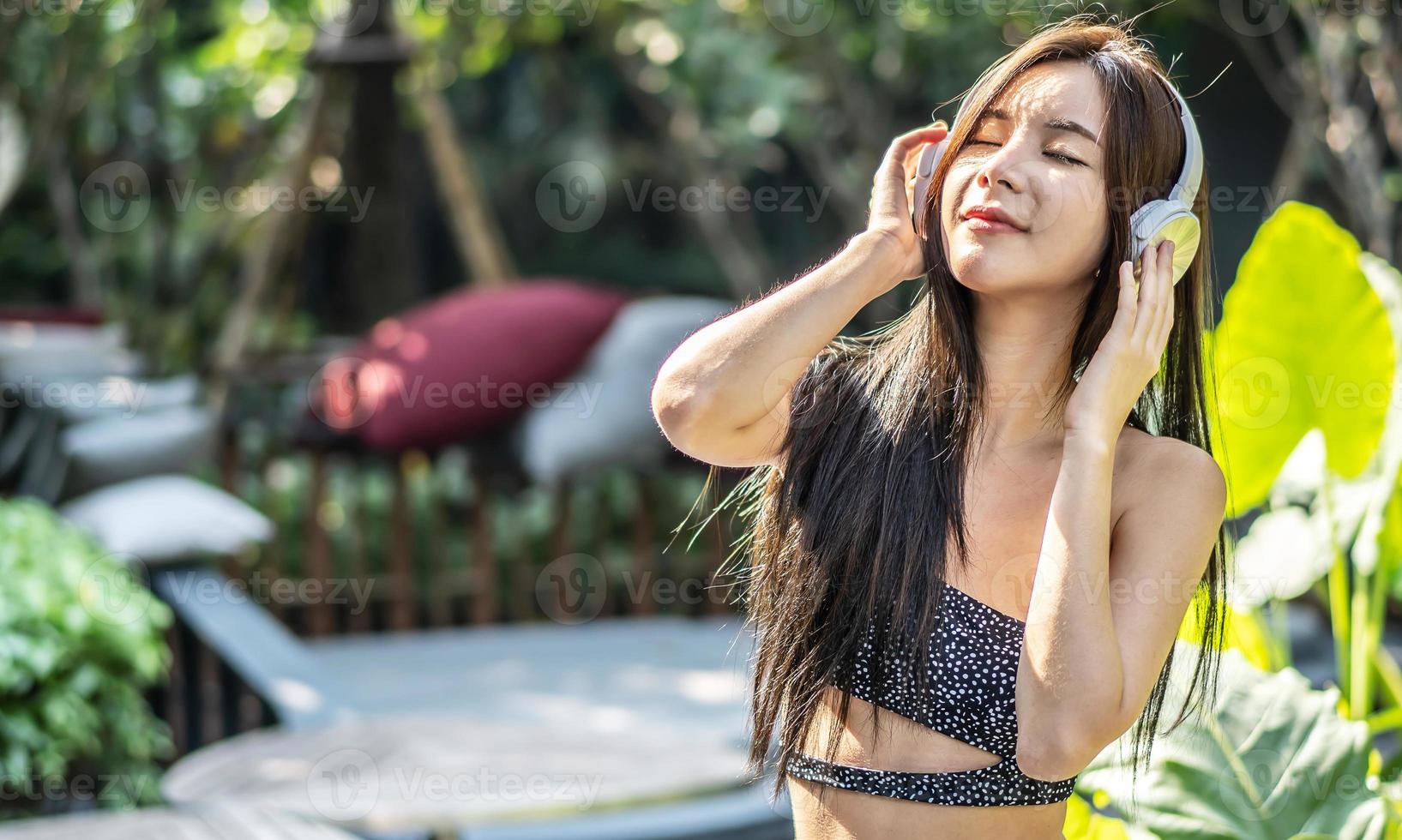 Relaxed beautiful young asian woman breathing deeply fresh air wearing headphones at the park in summer photo