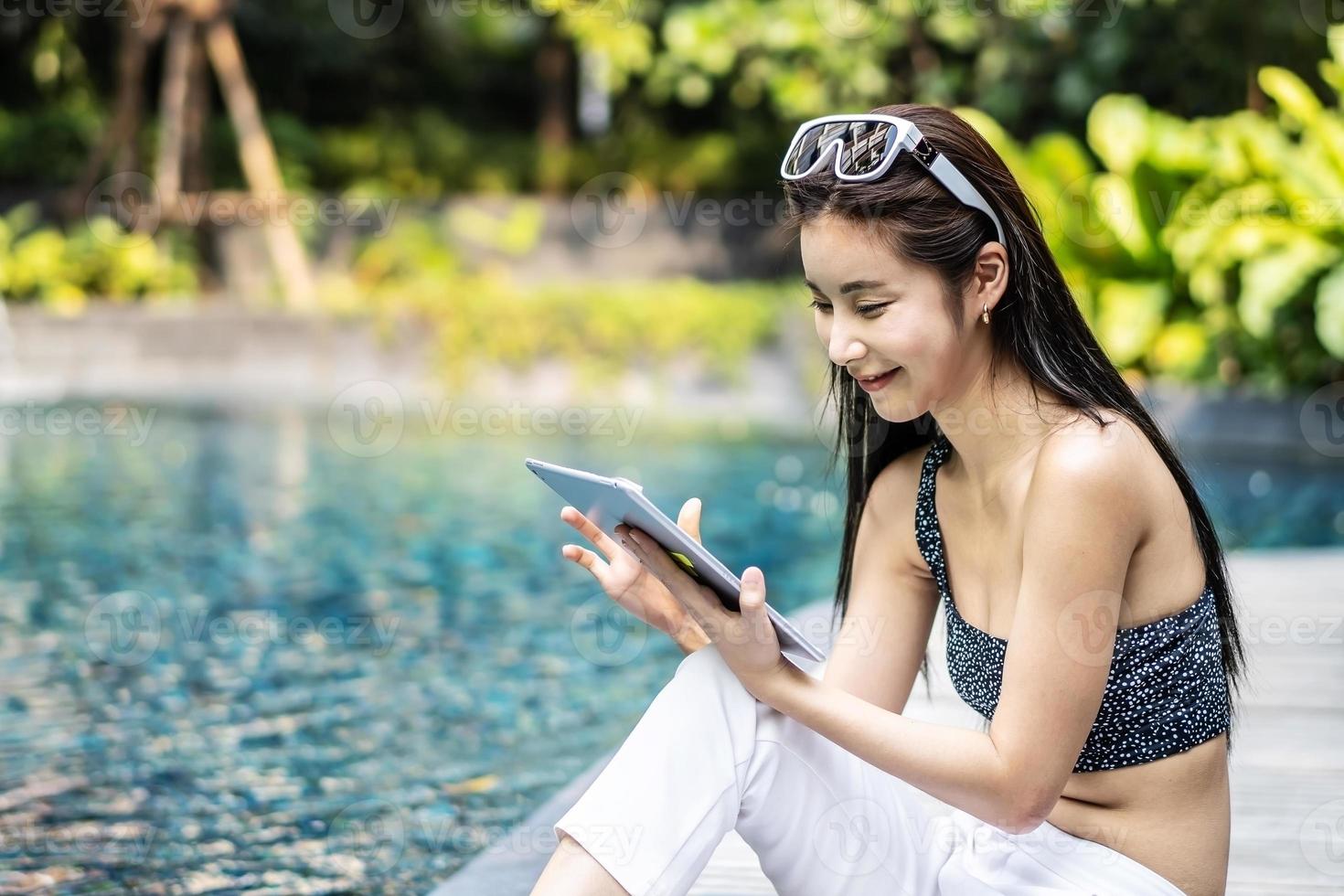 hermosa mujer asiática relajándose con el uso de una tableta digital al aire libre junto a la piscina foto
