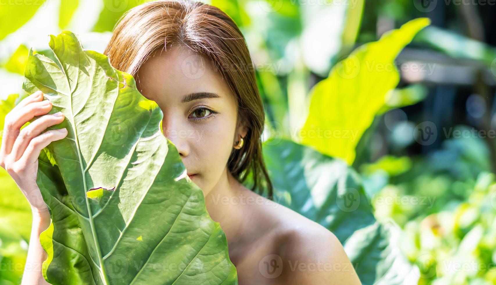Portrait of a Beautiful asian young woman with natural makeup holds a big green leaf on a blurred green background. Spa and wellness. Youth, teens and skin care concept photo