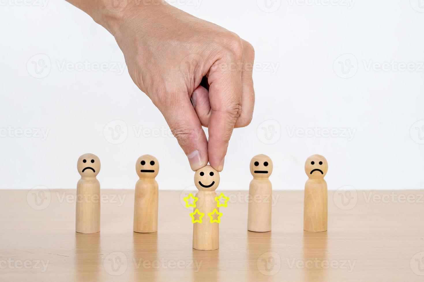 primer plano de la mano de un hombre de negocios que elige una cara sonriente en una muñeca de madera, los mejores servicios comerciales excelentes que califican la experiencia del cliente. concepto de encuesta de satisfacción, satisfacción de 5 estrellas. foto