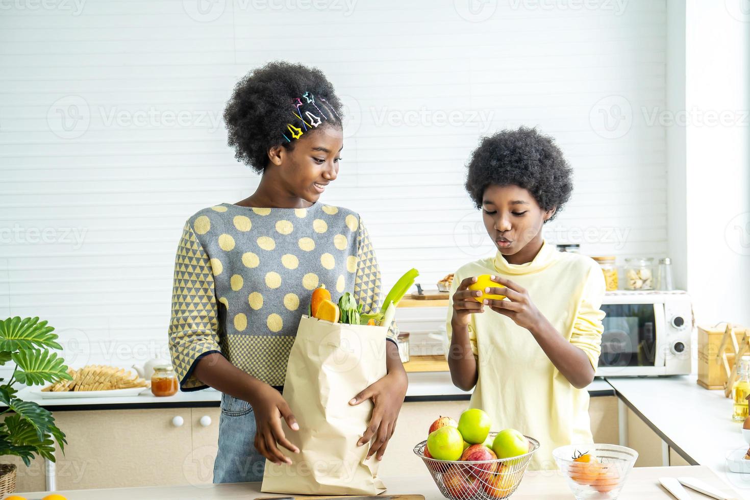 Two adorable African American children, brothers and sisters, have just returned from the market. and took the tomato, carrot, lemon out of the paper bag to cook, health concept photo