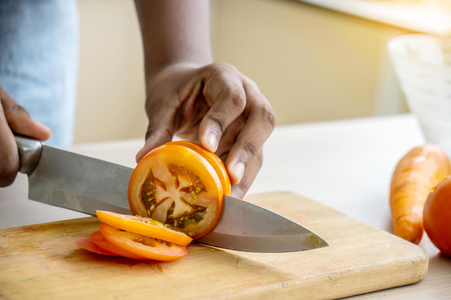 Close up of hand african american girl chopping  tomatoes on cutting board with knife in kitchen photo