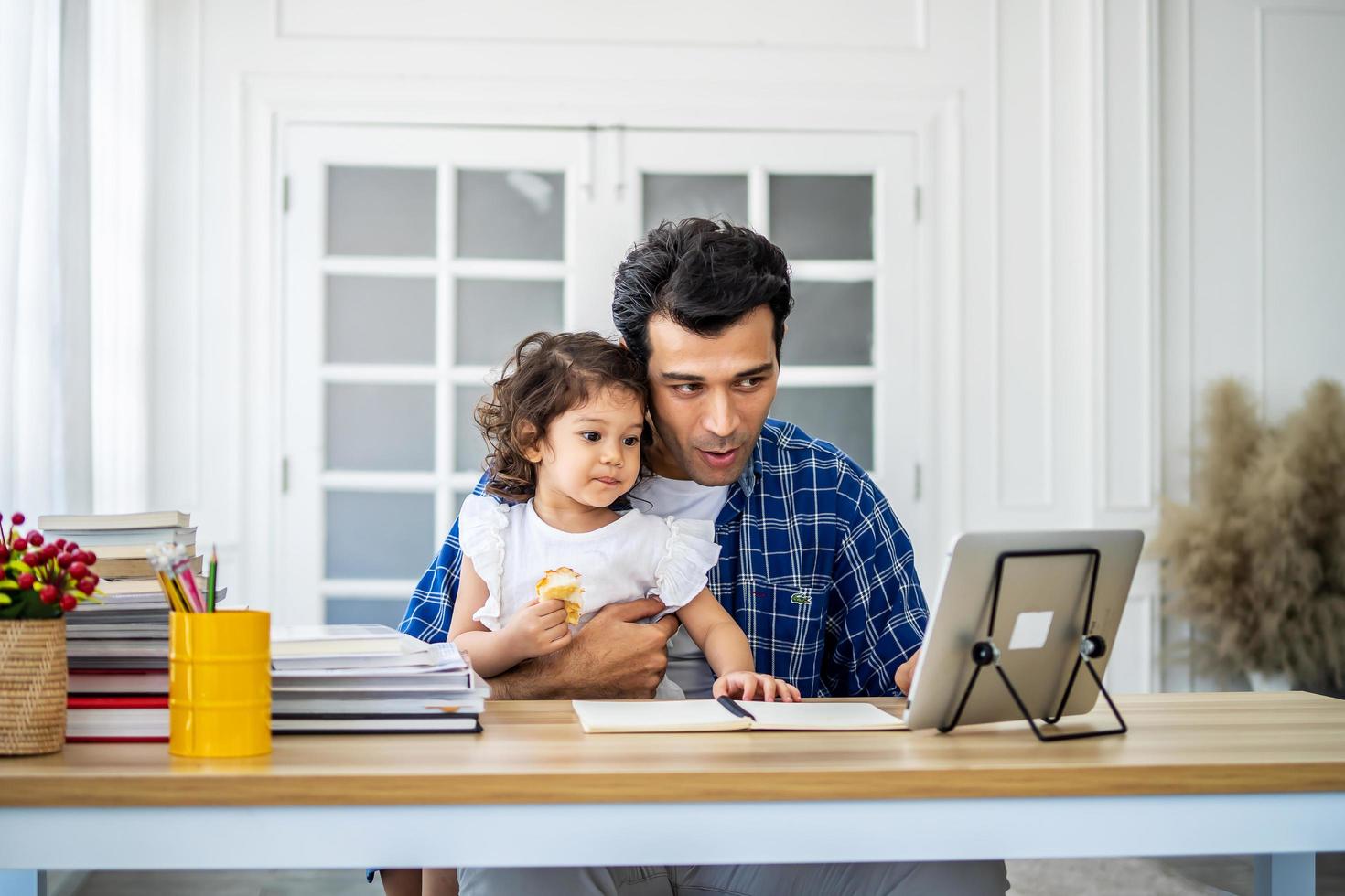 Father and daughter at home eating a slice of pizza food online together with her mother in video conference with digital tablet for a online meeting in video call for social distancing photo