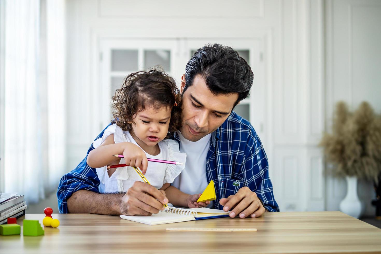 retrato de un joven padre enseñando el estudio de sus lindas hijas. emocionada y sonriente niña pequeña que disfruta aprendiendo con un padre agradable en casa. educación infantil, concepto de educación en el hogar foto