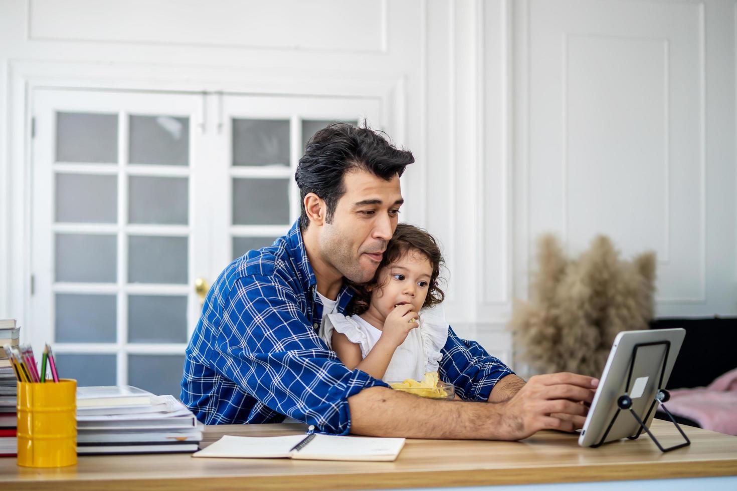 Father and daughter at home eating a slice of pizza food online together with her mother in video conference with digital tablet for a online meeting in video call for social distancing photo