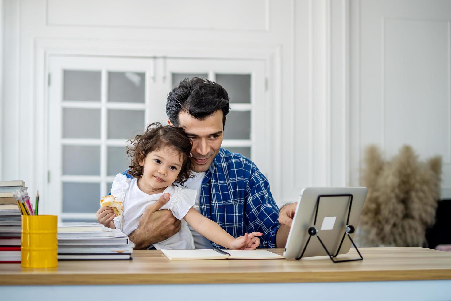 Father and daughter at home eating a slice of pizza food online together with her mother in video conference with digital tablet for a online meeting in video call for social distancing photo