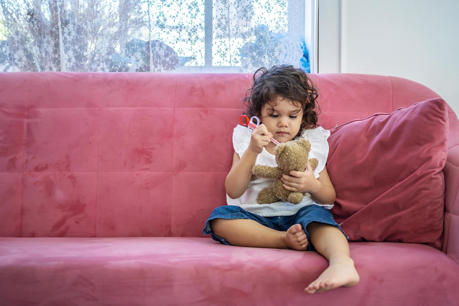 A little cute girl enjoy playing toy injection syringes toy on the teddy bear on the sofa in the home, education time at home photo
