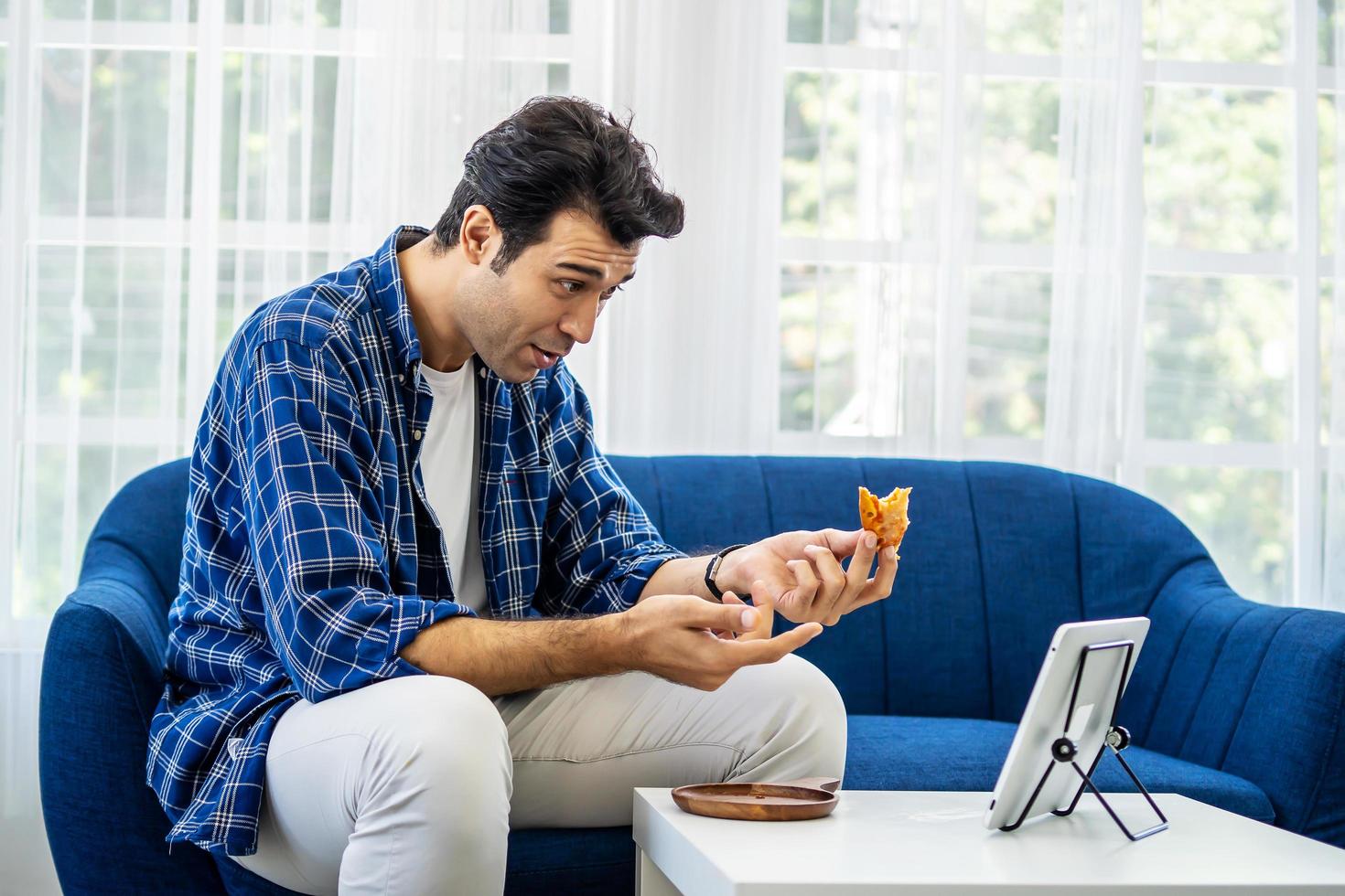 hombre caucásico en casa comiendo una rebanada de pizza en línea junto con su novia en videoconferencia con tableta digital para una reunión en línea en videollamada para distanciamiento social foto