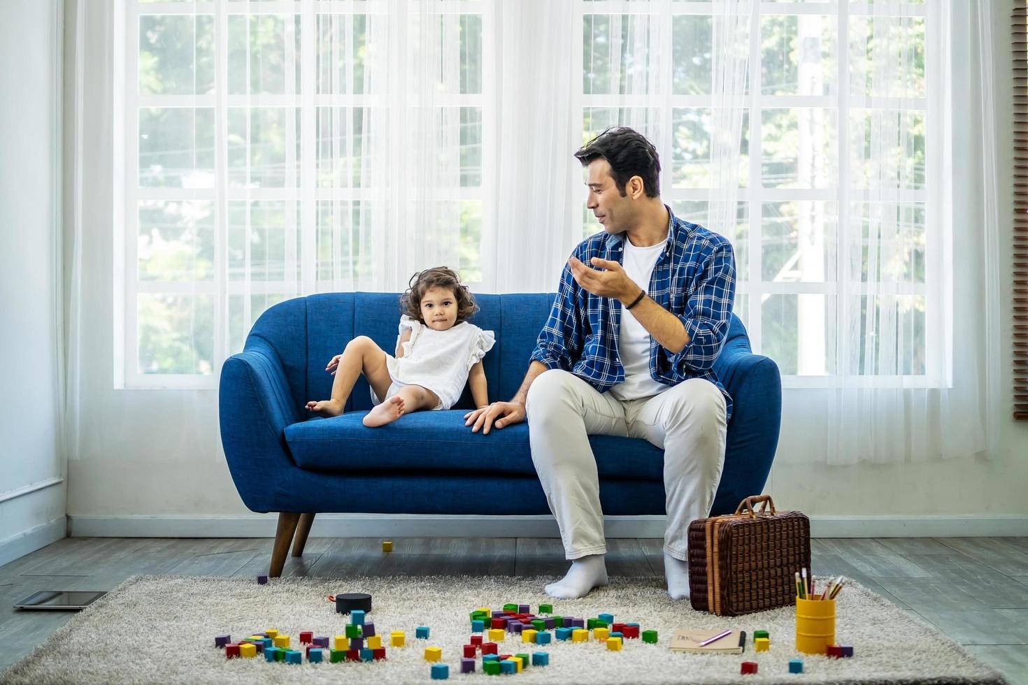 joven padre atractivo hablando con su pequeña hija linda después de jugar con bloques de madera, familia feliz pasando tiempo libre el fin de semana juntos foto