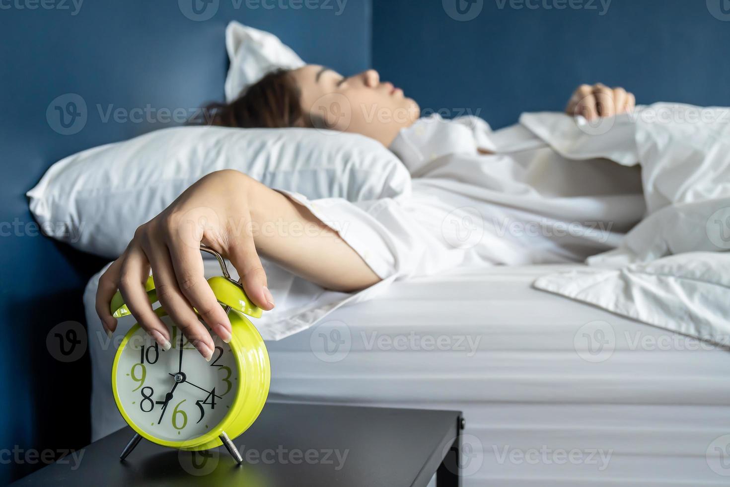 Close up sleepy woman stretching hand to ringing alarm willing turn it off, pressing button, woken by signal, lying under blanket in cozy bed, Early wake up, not getting enough sleep concept photo