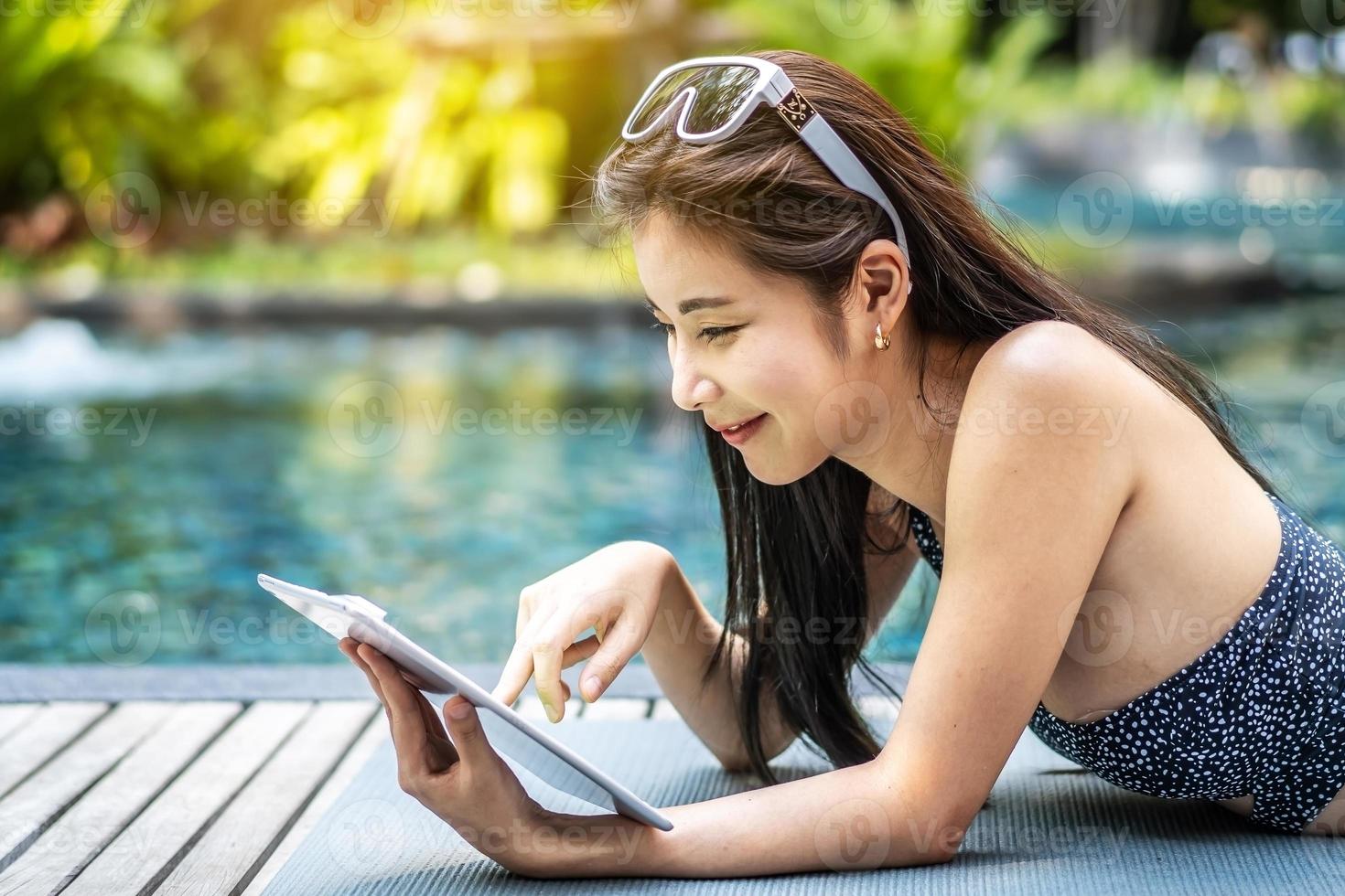 Beautiful asian woman relaxing with using digital tablet computer outdoors by the swimming pool photo