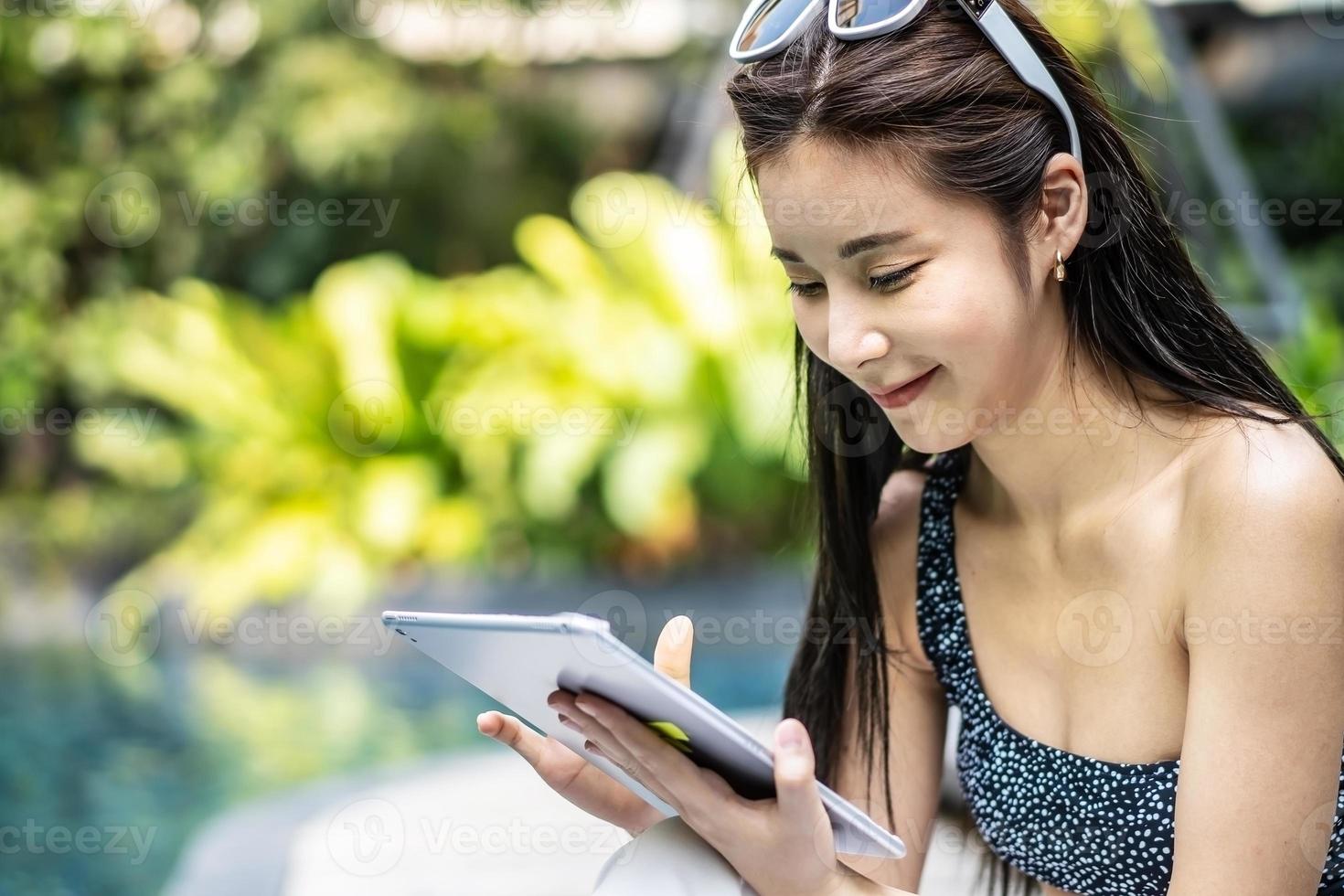 Beautiful asian woman relaxing with using digital tablet computer outdoors by the swimming pool photo