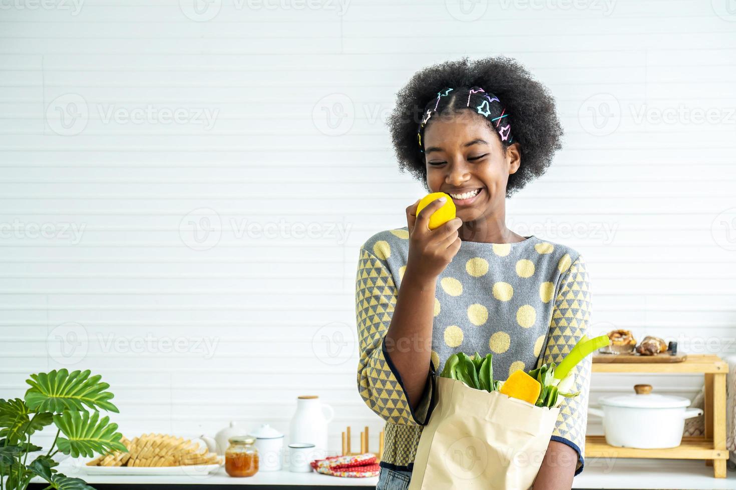 joven feliz mujer afroamericana pelo afro acaba de regresar del mercado. y sacó el tomate, limón de la bolsa de papel para cocinar, concepto de salud foto