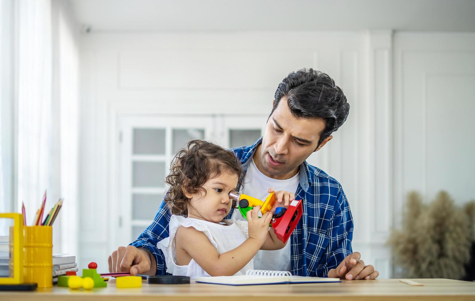 concepto de familia, paternidad e infancia - padre feliz e hija pequeña jugando con microscopio de juguete en la mesa en casa foto