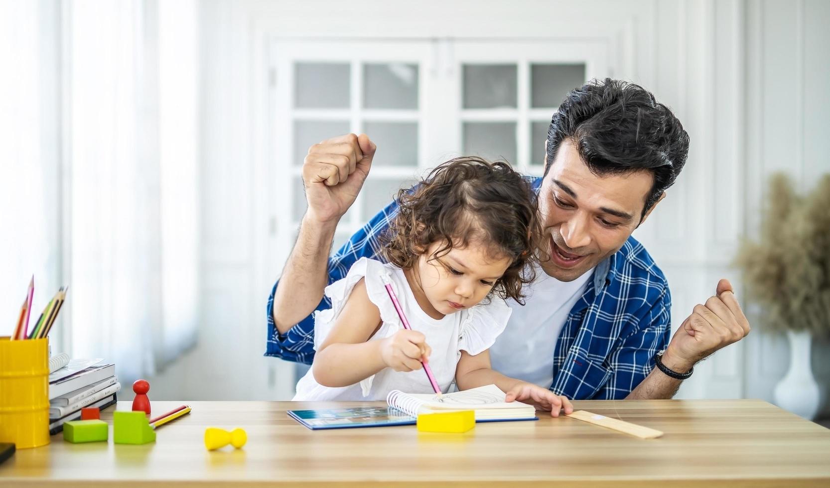 retrato de un joven padre enseñando el estudio de sus lindas hijas. emocionada y sonriente niña pequeña que disfruta aprendiendo con un padre agradable en casa. educación infantil, concepto de educación en el hogar foto