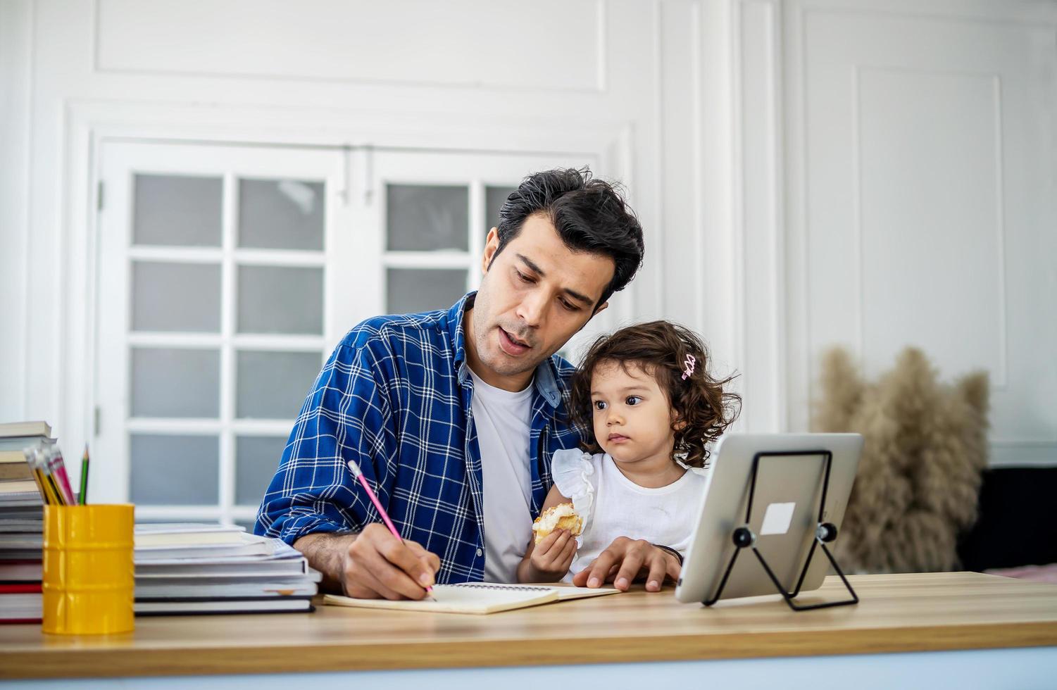 joven padre atractivo y pequeña hija linda viendo el video tutorial en la tableta y enseñando la tarea en casa con felicidad. foto