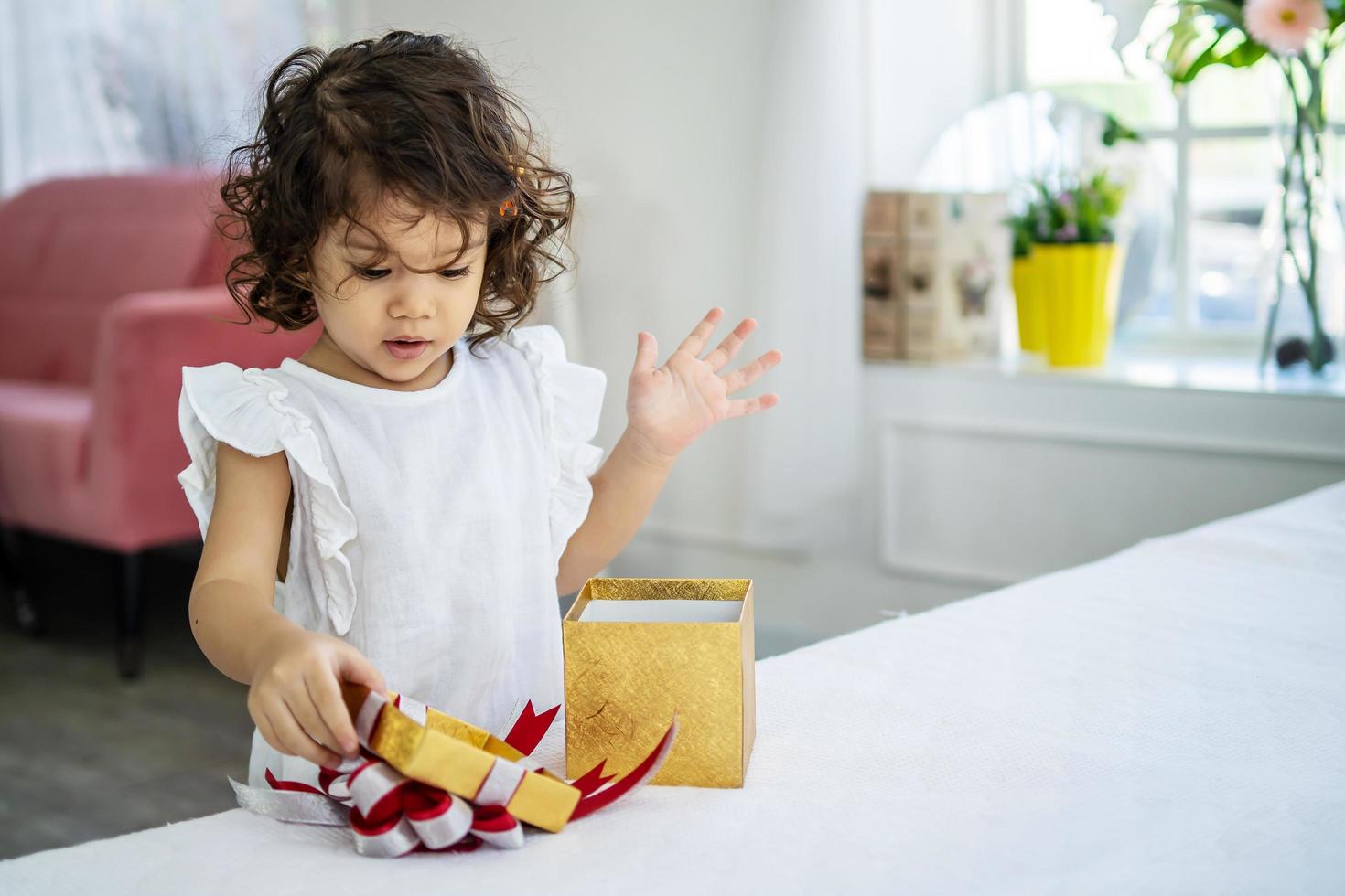 Portrait of adorable little girl opening birthday box gift and looking inside with surprised joyful facial expression photo