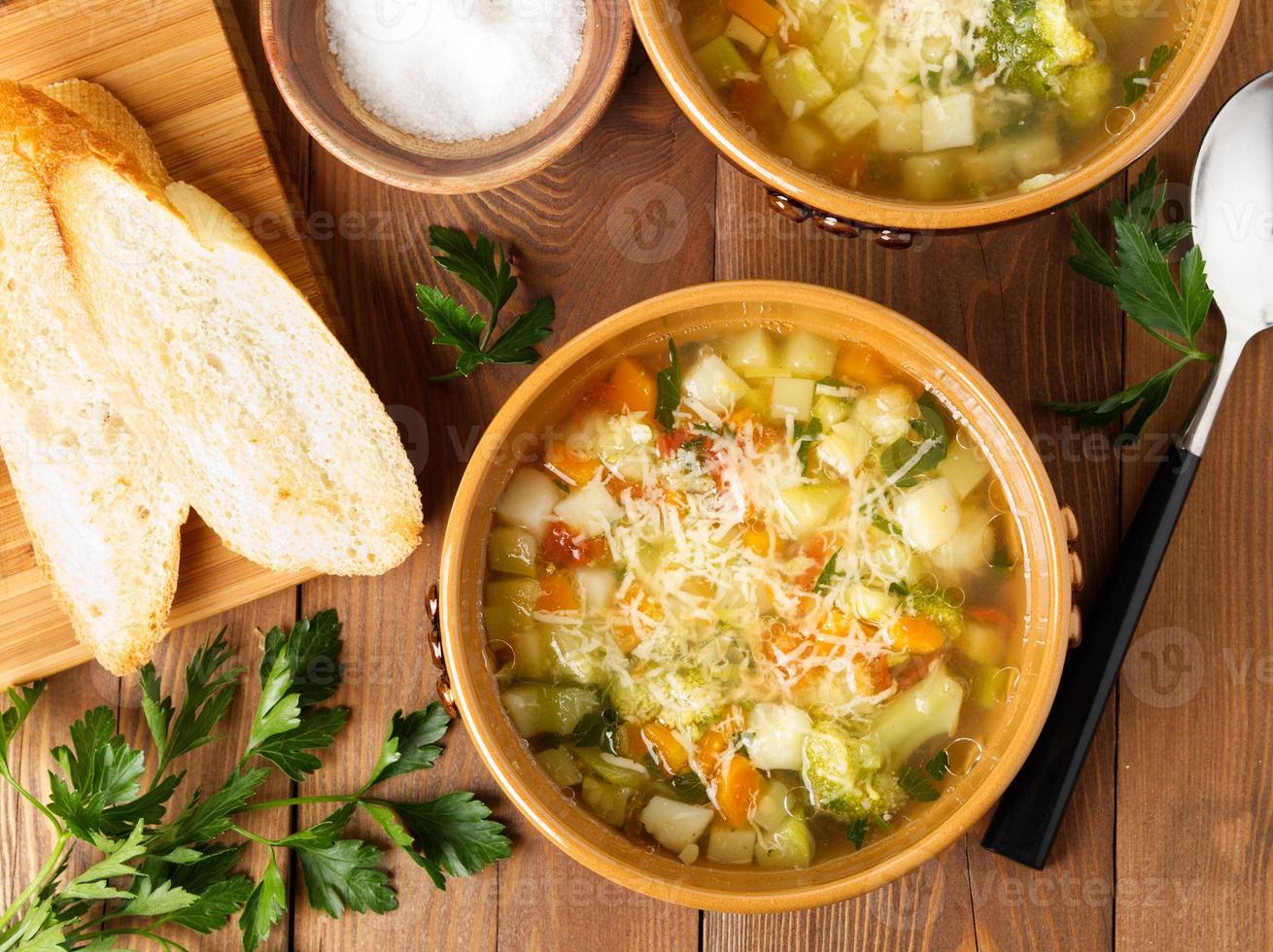 Two bowl of minestrone soup with toast on rustic wooden background, top view photo
