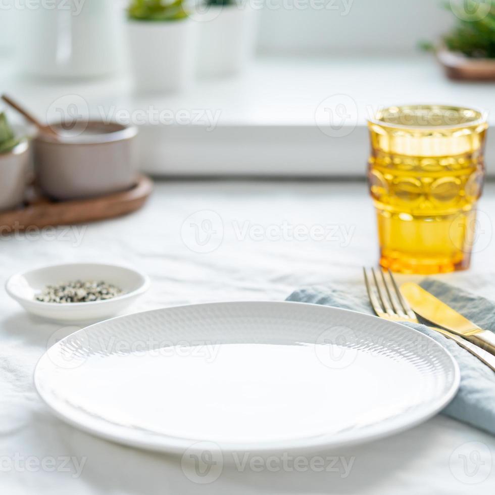 Side view of clean empty white plate, glass of water, fork and knife on white tablecloth photo