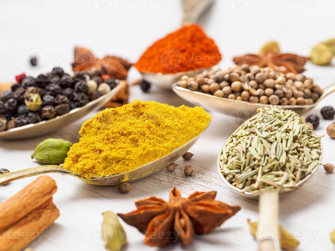 Mix of Indian spices in spoons on white wooden table, side view, selective focus, macro. Seasonings turmeric, close up photo
