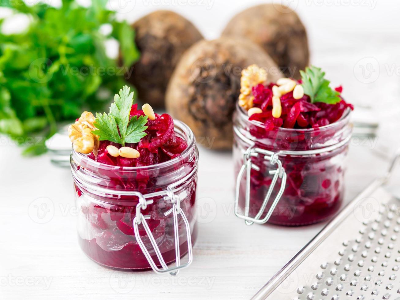 Fresh salad of grated boiled beetroot in jars, white wooden background, side view. photo