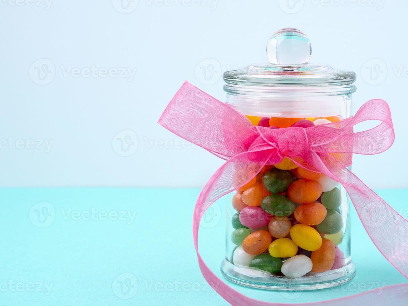 glass jar with sweets, candy, with a bow of pink ribbon on a turquoise table photo