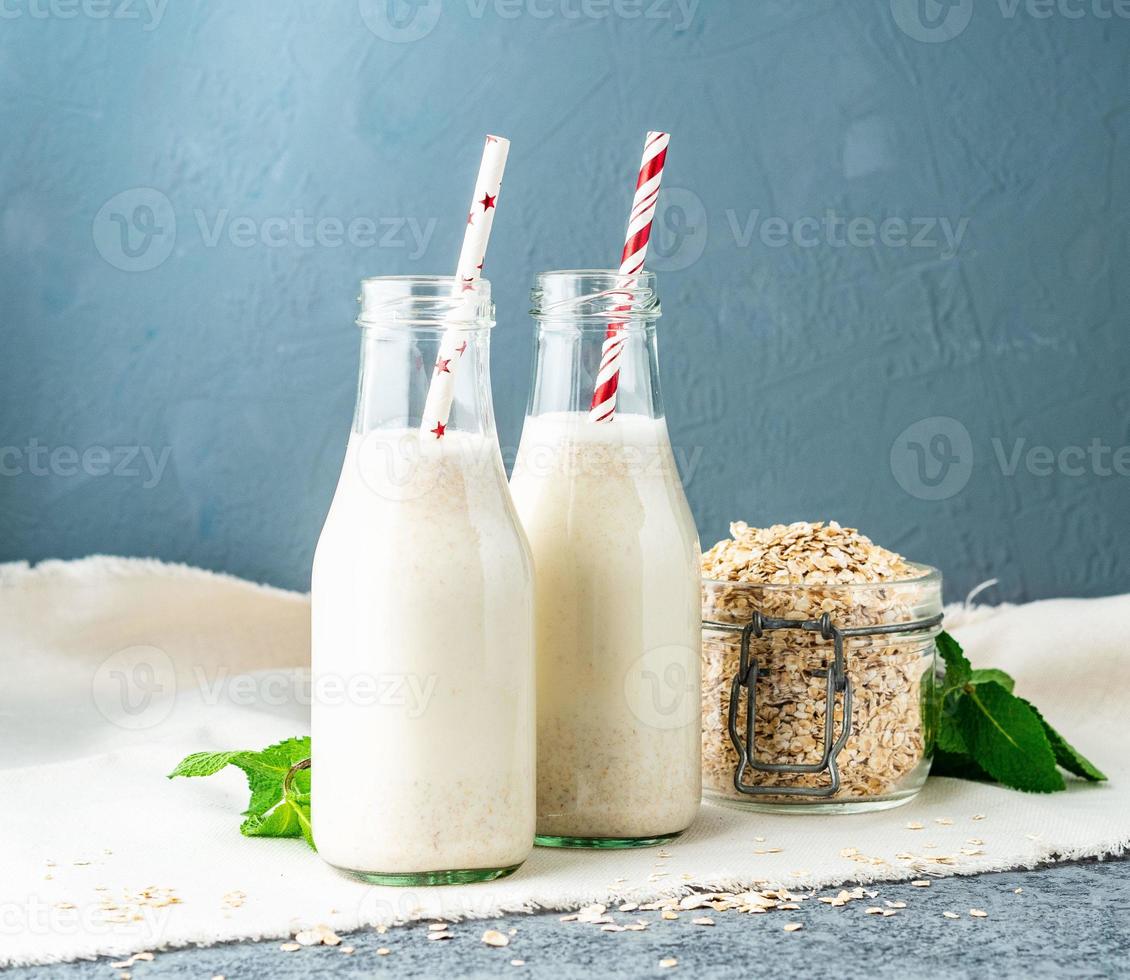 batido con avena, menta para un desayuno saludable. leche de avena en botella de vidrio con tubo sobre fondo de piedra oscura. foto