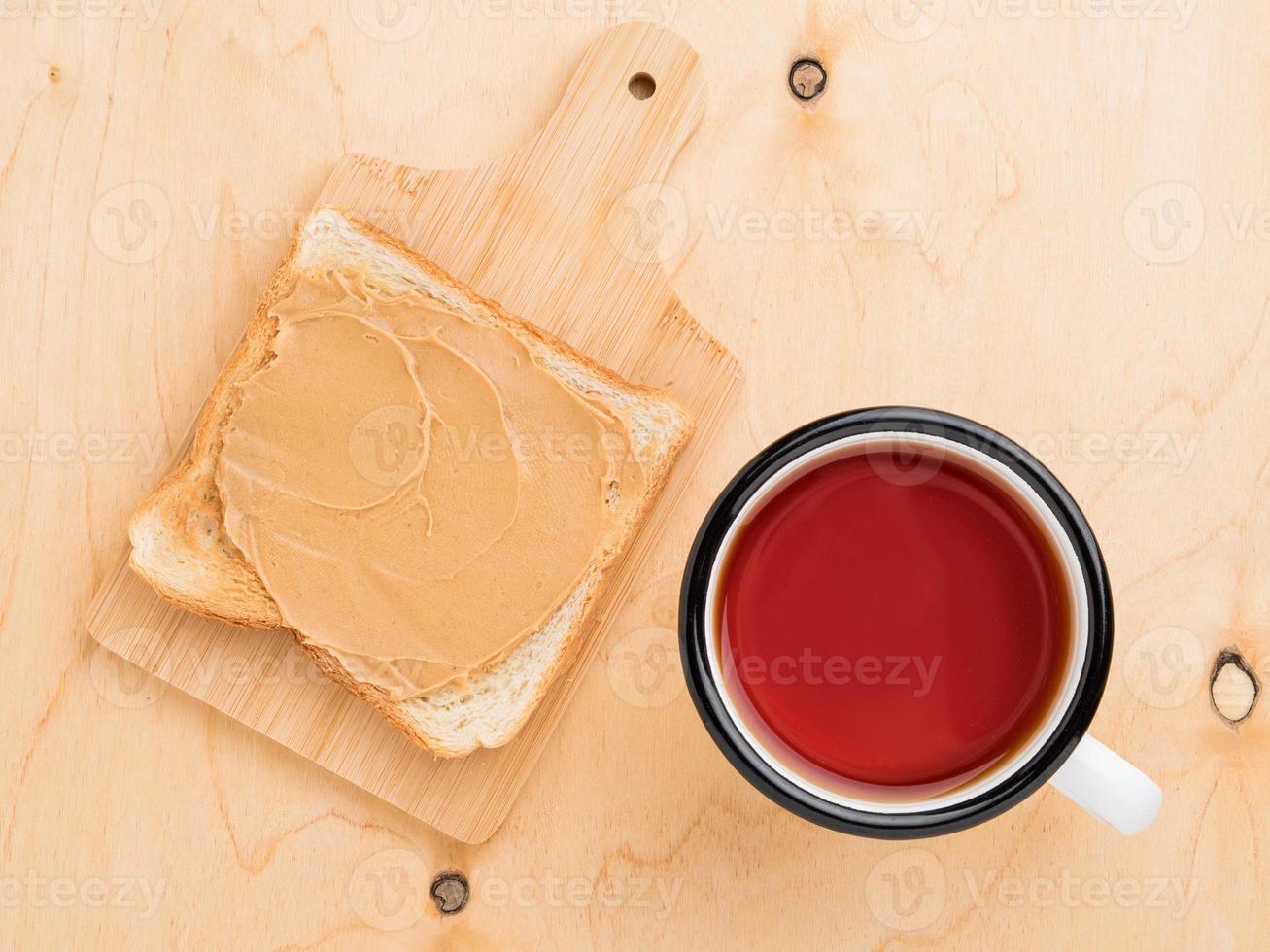 toast with peanut butter, spreading on sandwich, mug of tea on a beige wood background photo