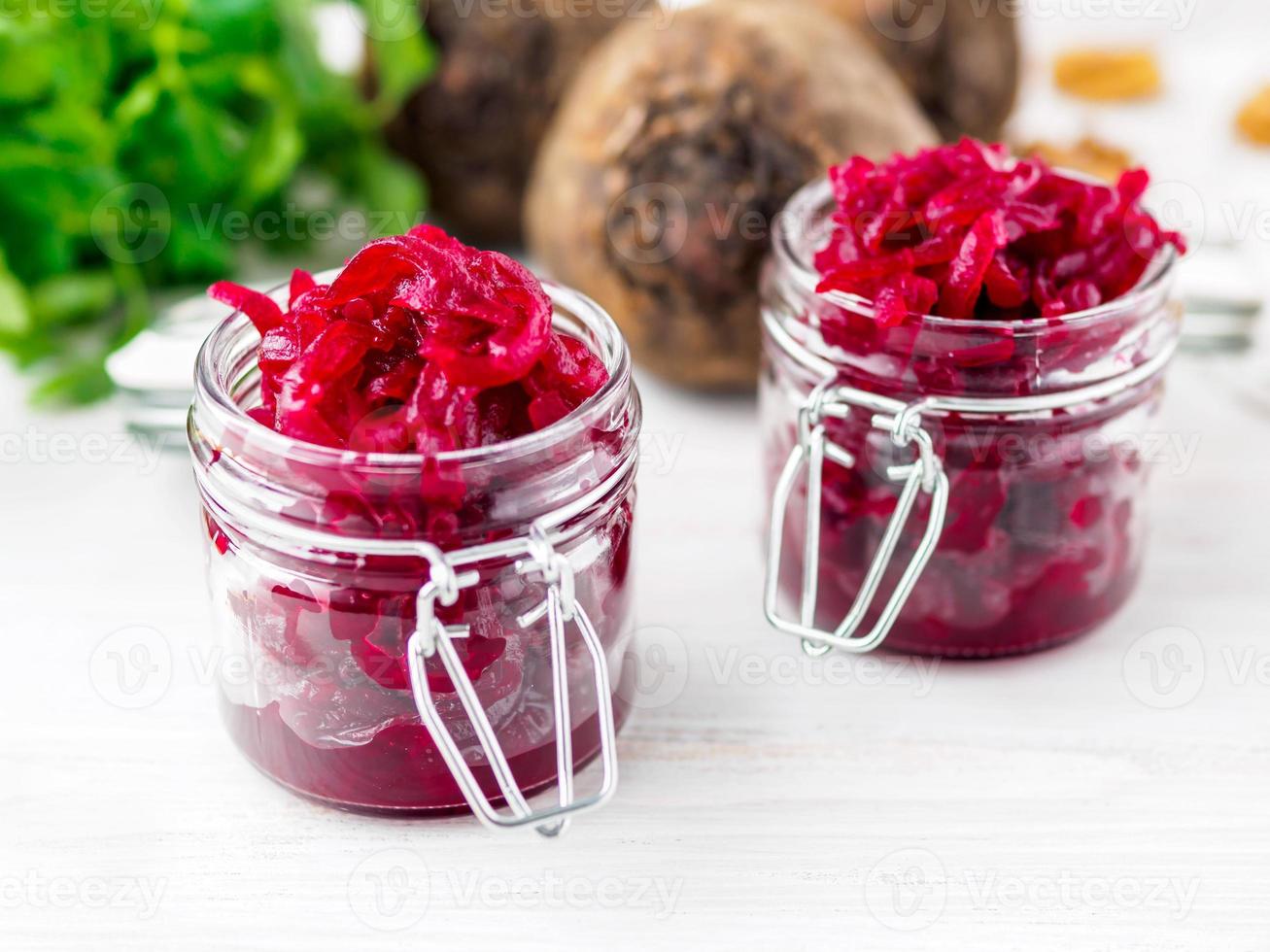 Fresh salad of grated boiled beetroot in jars, white wooden background, side view. photo
