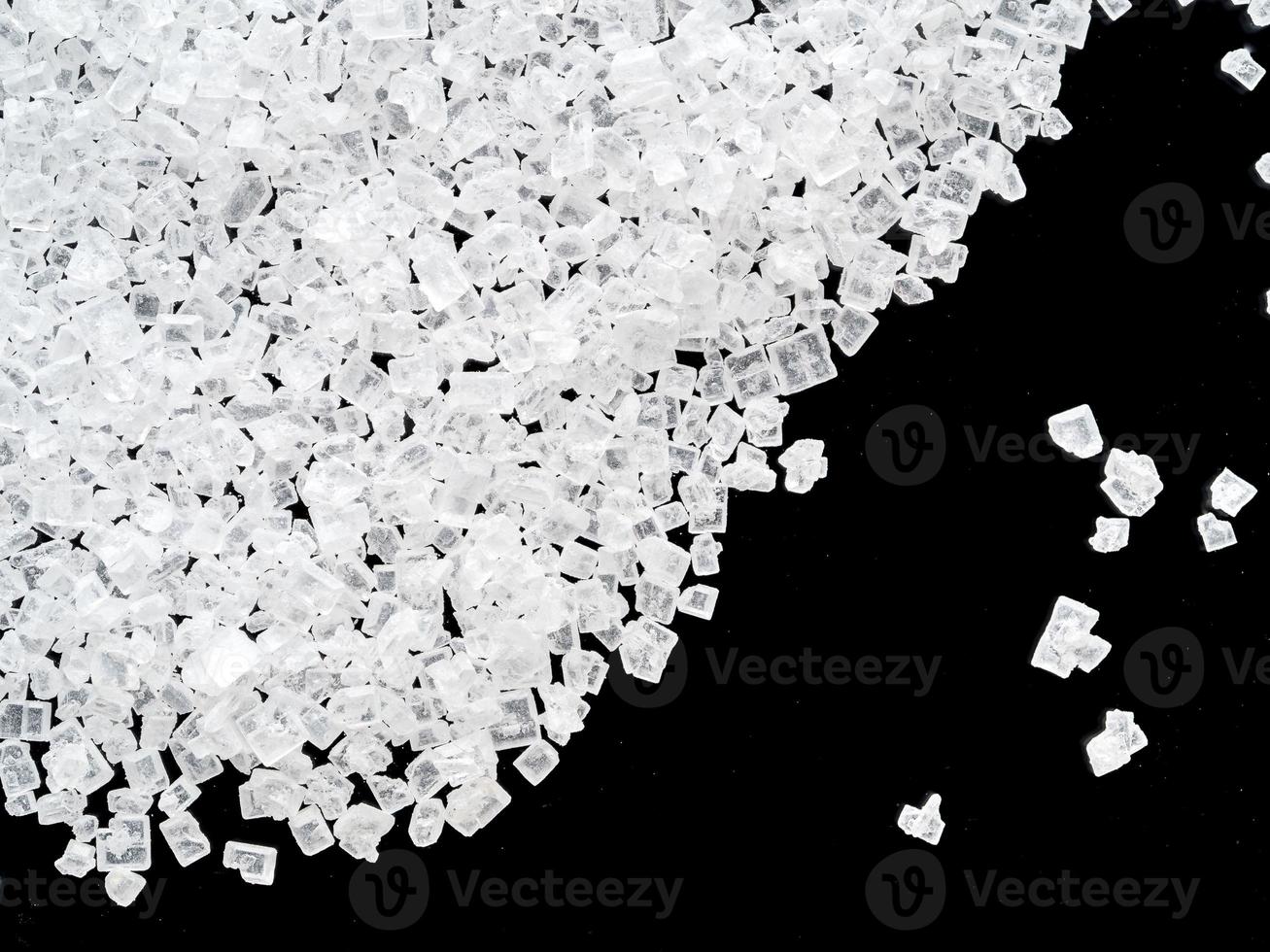 white crystals of sugar on black background, close-up, top view. photo