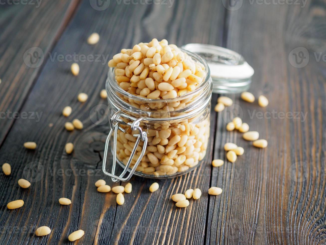 Side view of glass jar with a handful of pine nut, cedar nuts on a wooden background, selective focus photo
