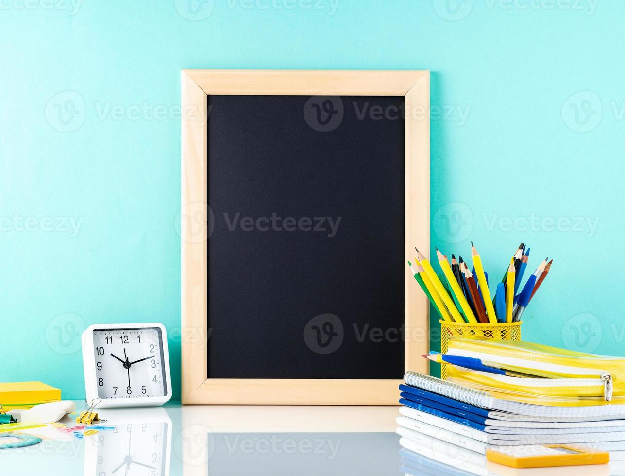 Chalkboard and school supplies on white table by the blue wall. Side view, empty space. Back to school concept. photo