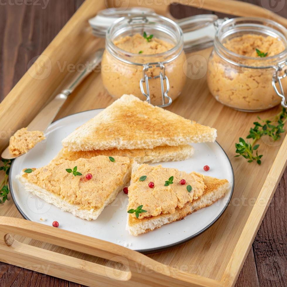 Fresh homemade chicken pate on toasted bread on tray over rustic background, side view photo