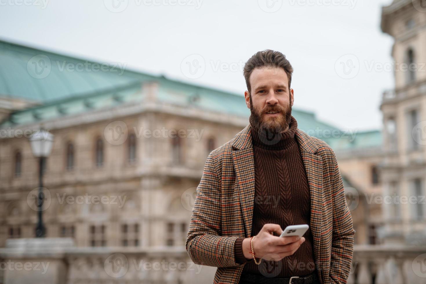 Young man holding a smartphone front of building. Creative businessman in historical city area. photo