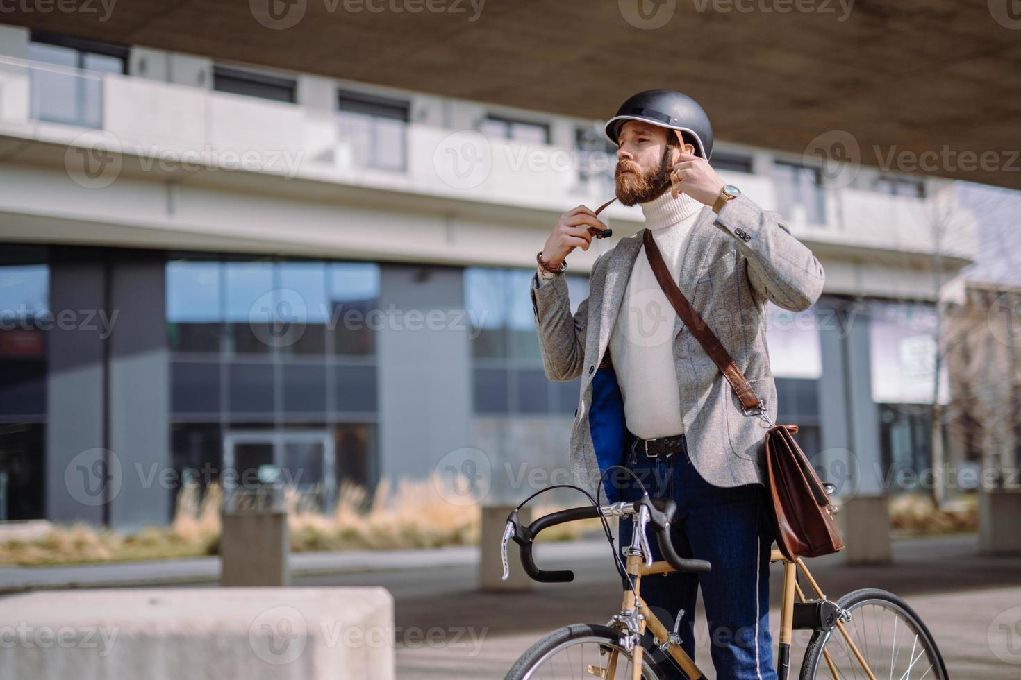 joven empresario se está poniendo casco antes de andar en bicicleta. viajar al trabajo. seguridad y transporte ecologico foto