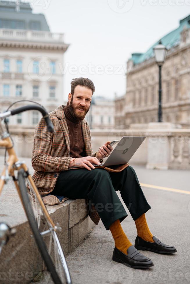 hombre elegante sentado afuera con laptop y móvil. llamada en línea trabajando afuera foto