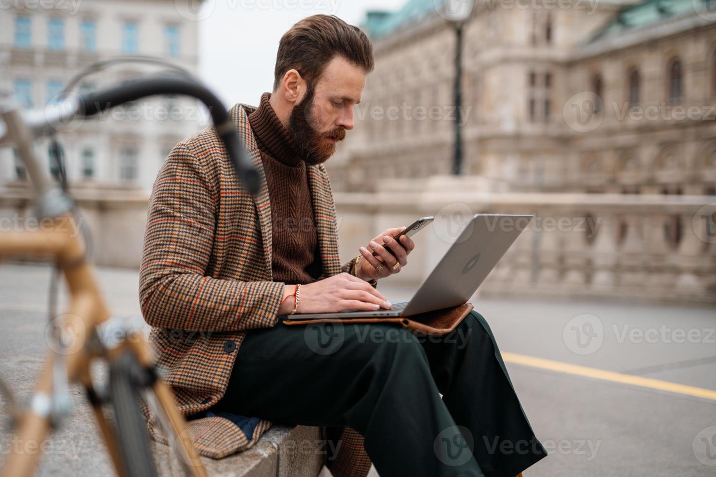 Creative freelancer sitting outside and working on laptop and mobile. Remote working. Video online call photo