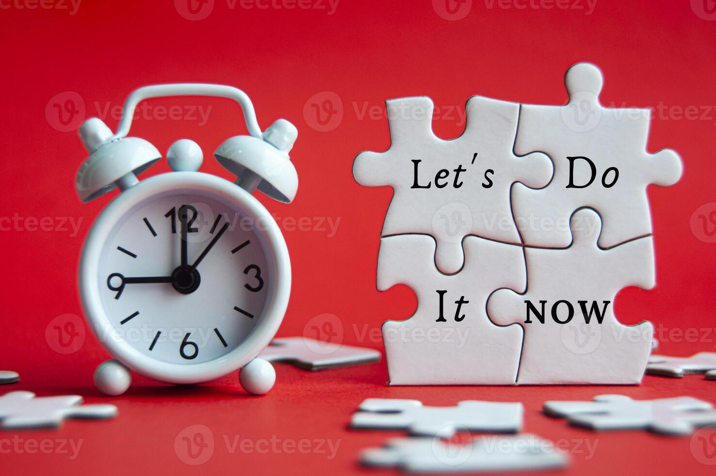 Let's do it now text on jigsaw puzzle with alarm clock pointing at 9 am on red cover background. photo