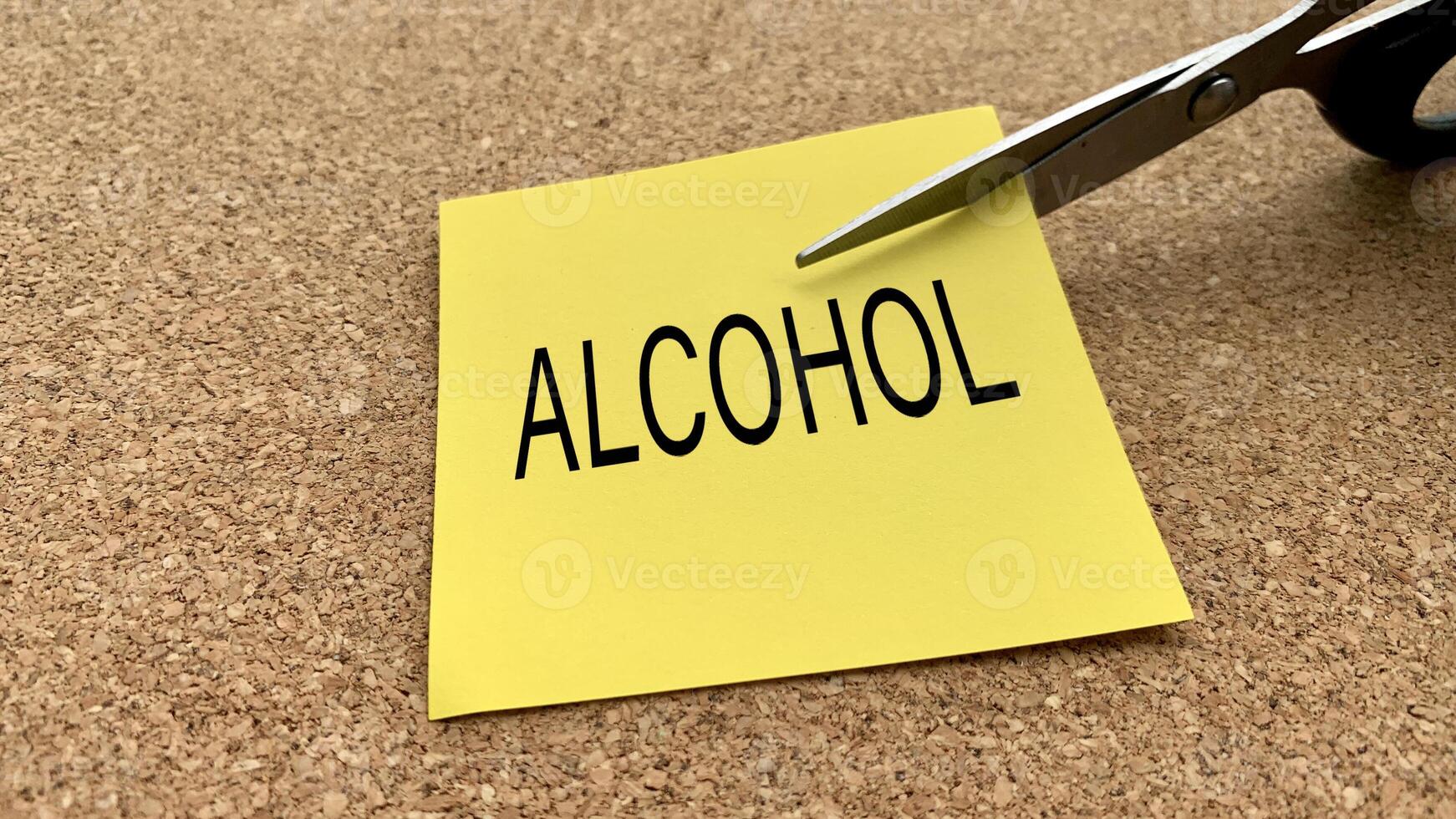 Scissors that cut yellow notepad with alcohol text on a wooden desk background. Spending concept photo